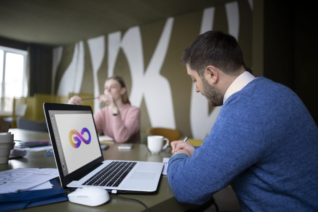 Hombre escribiendo en una libreta frente a una laptop mostrando un diseño gráfico colorido, en un entorno de trabajo colaborativo, reflejando servicios de branding y diseño digital de WeRise Performance.